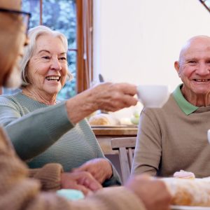 Toast, tea party and a group of elderly people in the living room of a community home for a social. Friends, smile or cheers with happy senior men and women together in an apartment for a visit